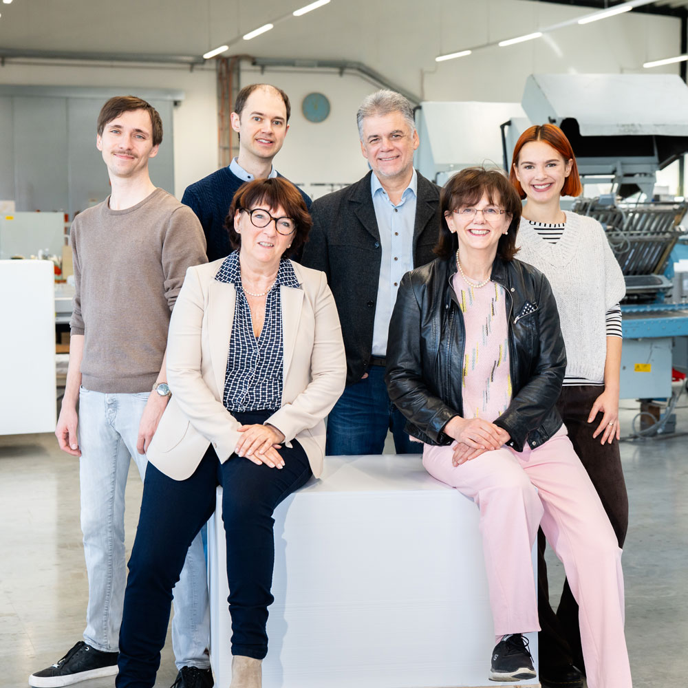 Ein Gruppenfoto von der Familie Kelly. Links angefangen mit Daniel Kelly, daneben Peter Kelly Jun., Geschäftsführer Peter Kelly und Maja Kelly stehend und Alexandra Kelly sowie Jutta Kelly sitzen auf einem weißen Block mit einem Bein. Alle Personen lächeln in die Kamera.