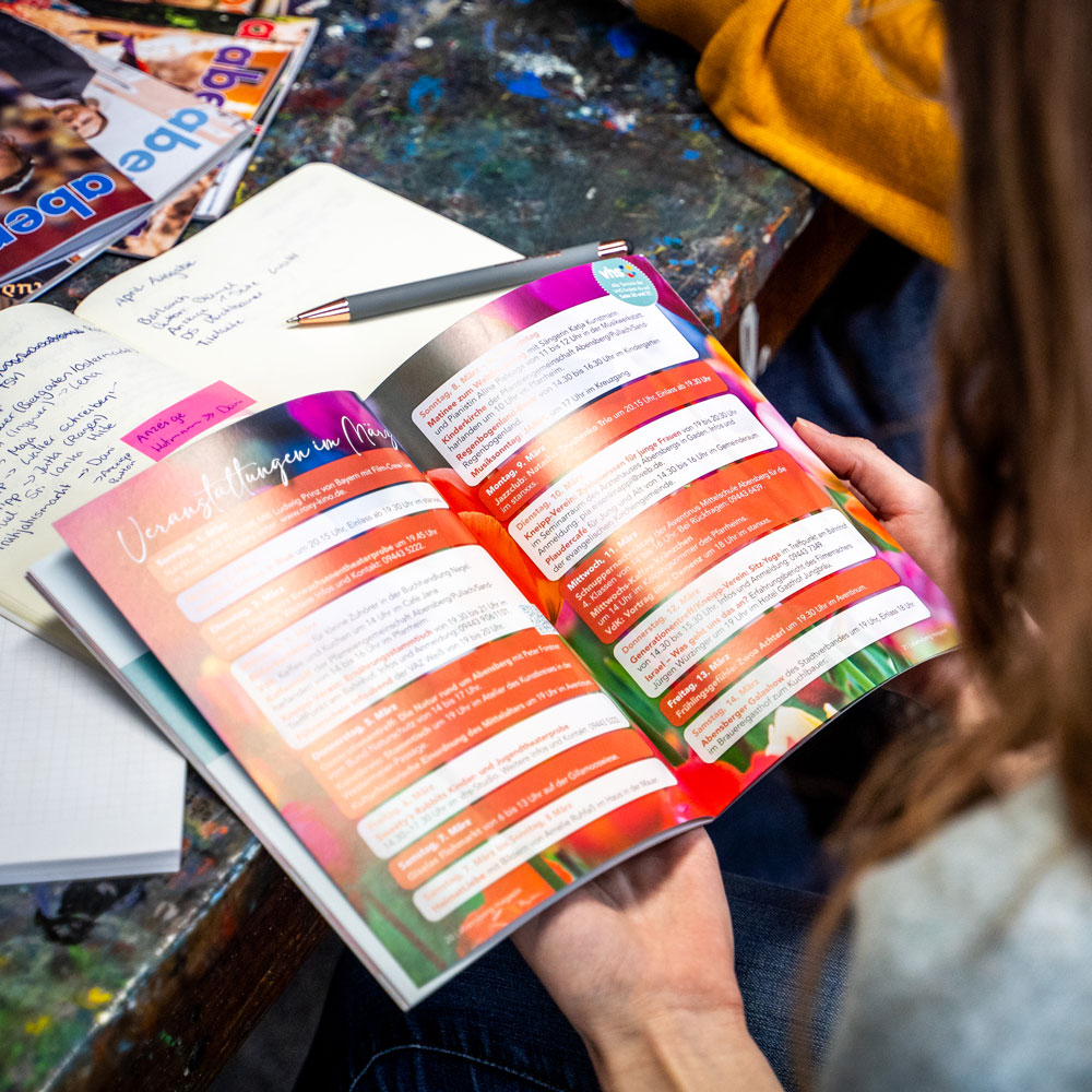 Oversholder Aufnahme von einer Frau, die ein sehr buntes Magazin mit weiß-roten Boxen, in der Hand hält und ließt.