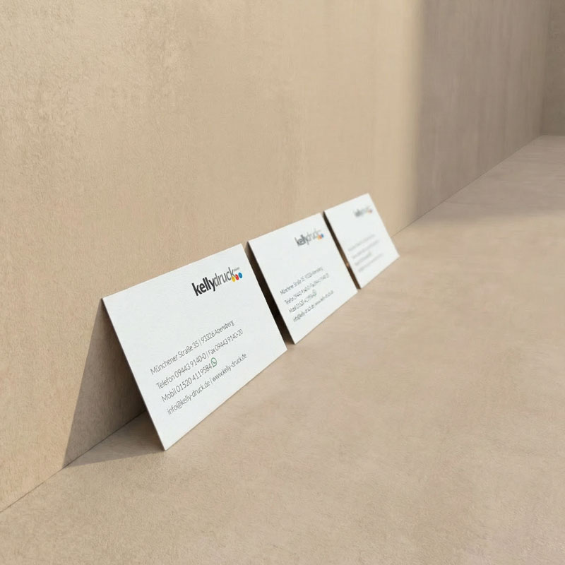 3 Visitenkarten mit der Aufschrift "Kelly-Druck" lehnen an einer grauen Wand.