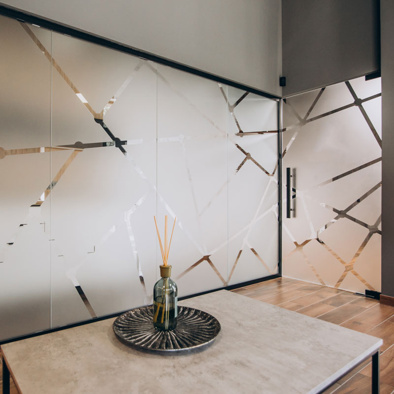 Ein Raum mit einer Glasfront, die mit einer geometrisch gemusterten Milchglasfolie dekoriert ist.